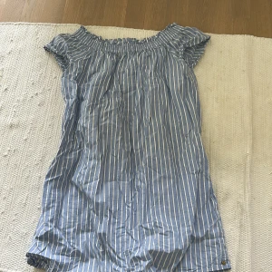 Blåvit randig klänning från Scotch & Soda - Säljer en blå och vit randig klänning från Scotch & Soda. Klänningen har korta ärmar och resår vid axlarna för en offshoulder-look. Perfekt för varma dagar och enkel att styla med sneakers eller sandaler.