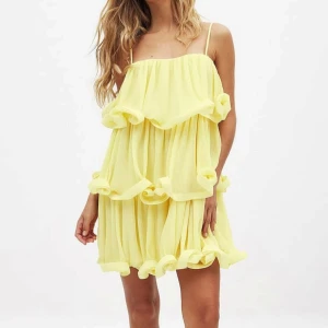 Gul volangklänning med tunna axelband nakd  - Superfin gul klänning med volanger och tunna axelband. Klänningen är plisserad och har en luftig, flowy passform med flera lager volangdetaljer. Perfekt för sommarens alla tillfällen och ger en riktigt glad vibe.