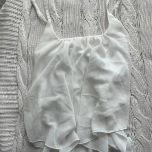 Vit volangig linnetopp - Säljer en vit linnetopp med volangdetaljer och tunna axelband. Toppen är luftig och har en flowy känsla, perfekt för varma dagar. Materialet är tunt och lätt, vilket ger en elegant look.