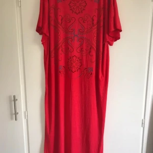 Röd koftan med mönster - Säljer en röd koftan med korta ärmar och dekorativt mönster framtill. Klänningen har en lös passform och är perfekt för dig som gillar färgstarka plagg med unika detaljer.