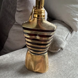 Jean Paul Gaultier Le Male Elixir Parfum - Säljer en lyxig parfym från Jean Paul Gaultier, Le Male Elixir. Flaskan är formad som en manlig torso i guld med svarta ränder och levereras i en matchande guldfärgad burk. Parfymen är tillverkad i Frankrike och har en unik, elegant design. Parfymen är använd lite men det finns minst 105 ml kvar i flaskan!