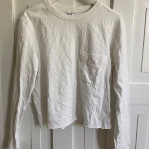 Vit långärmad tröja från Uniqlo  - Säljer en klassisk vit långärmad tröja från Uniqlo U i storlek S. Tröjan har rund halsringning och en bröstficka. Avklippt nertill. Och en liten fläck som inte gått bort på magen.