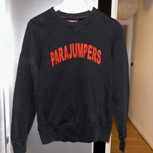 Svart fleece-tröja från Parajumpers - Svart långärmad fleece-tröja från Parajumpers med röd logotyp framtill och patch på ärmen. Klassisk rund halsringning och ribbade muddar. 