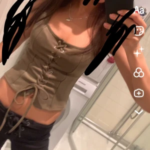  korsettopp med snörning - Säljer en olivgrön korsettopp med snygg snörning framtill. Toppen är croppad och har en figurnära passform med tunna axelband. Säljer då den inte kommer till använding❤️