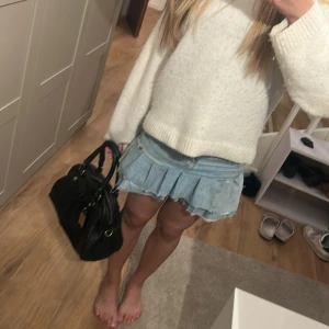 Jeanskjol med volanger - Säljer en ljusblå jeanskjol med volanger och råa kanter. Kjolen har klassiska jeansdetaljer som fickor och knappstängning framtill. Perfekt för dig som gillar en trendig och avslappnad stil.