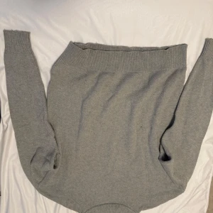 Ljusgrå stickad tröja med bred krage - Mysig ljusgrå stickad tröja med bred ribbad krage och långa ärmar. Perfekt för kyligare dagar och enkel att matcha med olika outfits. Tröjan har en klassisk och stilren design.