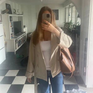 Beige trenchcoat  - Säljer en stilren beige trenchcoat från stradivarius med knytskärp i midjan och klassisk krage. Jackan har långa ärmar och knappar framtill. Perfekt för vår och höst.bra skick storlek xs