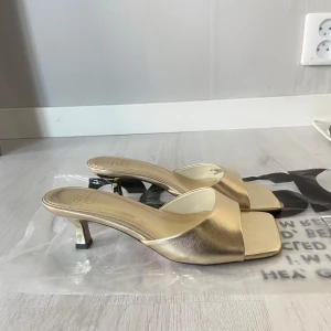 Guldiga klack-sandaler med öppen tå - Säljer populära guldiga mules från Asos, aldrig använda då jag valde ett par andra till min bal!.🤍