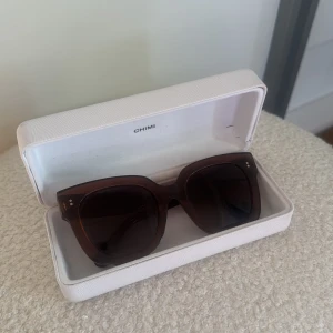 Bruna solglasögon från CHIMI - Snygga solglasögon från CHIMI i modellen COCO #008. Glasögonen har en mörkbrun, transparent båge och mörka linser. Perfekta för att ge en cool touch till din stil.