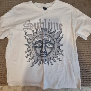 Vit Sublime t-shirt från H&M Divided - Vit t-shirt från Divided med stort Sublime-tryck framtill. T-shirten har rund hals och korta ärmar. Materialet är mjuk bomull, perfekt för en avslappnad stil.