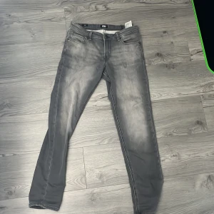 Grå slim fit jeans från Jack & Jones - Säljer ett par grå slim fit jeans från Jack & Jones, modell Glenn. Jeansen har klassisk femficksdesign, dragkedjegylf och snygga slitningar framtill och baktill för en cool look. Strl w 28 l 30