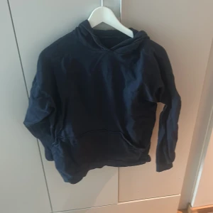 Mörkblå hoodie - Mörkblå hoodie med huva och magficka. Klassisk modell med lång ärm och avslappnad passform. Perfekt för en chill vardagslook.