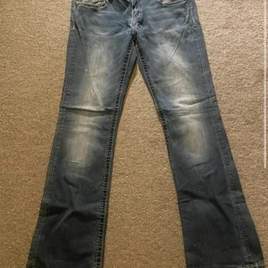 Blå bootcut jeans från Miss Me med paljettdetaljer - Säljer ett par blå bootcut jeans från Miss Me med snygga paljettdetaljer på bakfickorna. Jeansen har slitningar och en klassisk femficksdesign. Perfekta för dig som gillar en unik och trendig look. 2 små fläckar som knappt syns, dom är jätte små. Använda fåtal gånger annars jätte fina o bra.   ny pris runt 1000, pris kan diskuteras vid snabb affär 