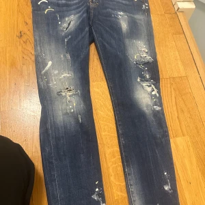 Mörkblå slitna jeans med detaljer - Säljer ett par mörkblå jeans med slitningar och färgstänk för en cool och trendig look. Jeansen har raka ben och klassisk femficksdesign. Perfekta för dig som gillar streetstyle.