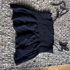 Svart croppad linnetopp från SHEIN - Säljer en svart croppad linnetopp från SHEIN med smockad överdel och tunna knytband vid axlarna. Toppen har en luftig passform nertill och är perfekt för varma dagar. Toppen är strl L men passar mig som är strl XS-S.