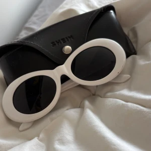 Vita ovala solglasögon - Säljer ett par trendiga vita solglasögon med tjock oval båge och svarta glas. Kommer med svart fodral. Aldrig använda men har ett litet märke på ena sidan, syns på bilden.