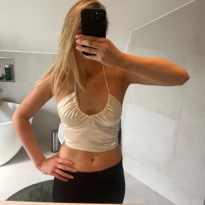 Krämvit croppad halterneck-topp - Säljer en krämvit croppad halterneck-topp med smala axelband som kan knytas på olika sätt framtill. Toppens material har en glansig finish och en rynkad detalj vid bysten. Köpt för ca 1 år sedan från ett UF företag och är handgjord. Sitter som en XS. Jag är 175 cm lång som referens. 💗💗💗