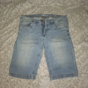 Ljusblå jeansshorts från FSBN - Ljusblå jeansshorts från FSBN med klassisk femficksdesign och knappgylf. Shortsens längd går till knäna och de har en avslappnad passform. Perfekta för varma dagar och enkel att matcha med olika toppar.