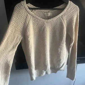 Beige stickad tröja med snörning från Hollister - Säljer en beige stickad tröja från Hollister med lång ärm och snygg snörningsdetalj i ryggen. Tröjan har en avslappnad passform och är perfekt för lager-på-lager-stil. Supermjuk och enkel att matcha med jeans eller kjol.