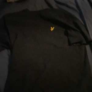 Svart tröja från Lyle & Scott med gul logga - Säljer en svart tröja från Lyle & Scott med deras klassiska gula fågellogga på bröstet. Enkel och stilren design som passar perfekt till vardags. Tröjan har normal passform och är tillverkad i mjukt material.