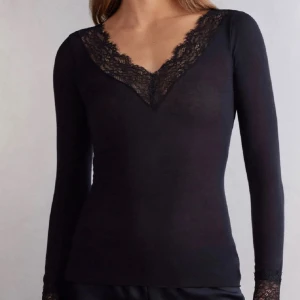 Svart långärmad topp med spets - Säljer en svart långärmad topp med djup v-ringning och fina spetsdetaljer längs halsringningen. Det finns två små hål på den ena armen och en liten hål på den andra men de syns knappt.