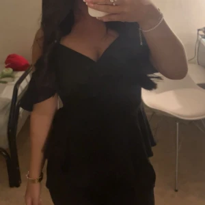 Svart off shoulder topp - Säljer en off shoulder med offshoulder-modell och volangdetaljer upptill. Toppen har en figurnära passform och omlott-skärning vid bysten. Perfekt för dig som gillar stilrena och eleganta plagg.