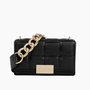 Svart axelväska med kedja från Ideal of Sweden - Snygg svart axelväska från Ideal of Sweden med flätad design och en chunky guldfärgad kedja. Väskan har en rektangulär form och en metallbricka framtill med logga. Perfekt för att lyfta din outfit.💗