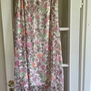 Blommig långklänning i bomull - Säljer en långklänning med blommigt mönster i rosa, orange och grönt på vit botten. Klänningen har en luftig passform och är perfekt för varma dagar. Materialet är mjuk bomull och modellen är ärmlös.