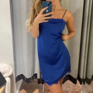 Blå kortklänning med spetsdetaljer - Säljer en blå kortklänning med tunna axelband och spetsdetaljer längs fållen. Klänningen är endast använd en gång och i topp skick. 