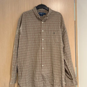 Rutig skjorta från Ralph Lauren - Säljer en klassisk rutig skjorta från Ralph Lauren i beige, rött och grönt. Skjortan har lång ärm, knappar framtill och broderad logga på bröstet. Tillverkad i 100% bomull för en skön känsla.