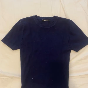 Mörkblå ribbad tröja från Gina Tricot - Säljer en mörkblå ribbad tröja från Gina Tricot. Tröjan har korta ärmar och rund halsringning. Perfekt till vardags och enkel att matcha med olika outfits.