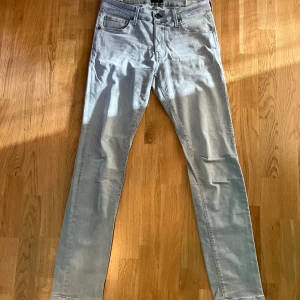 Gråa Jack and Jones Jeans - Säljer nu ett par jeans från Jack & Jones i modellen slim fit. Liten defekt på höger knä, utöver det i fint skick!