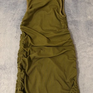 Olivgrön ribbad klänning från SHEIN - Säljer en olivgrön ribbad klänning från SHEIN i storlek XS. Klänningen har åtsittande passform och rynkade detaljer längs sidorna. Perfekt för dig som gillar en enkel men trendig look.