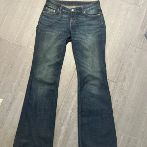 Weekday Nova Low Slim Bootcut Jeans - Mörkblå jeans från Weekday i modellen Nova Low Slim Bootcut. Byxorna har låg midja, klassisk femficksdesign och bootcut-ben. Perfekta för dig som gillar en tidlös och snygg jeansstil.