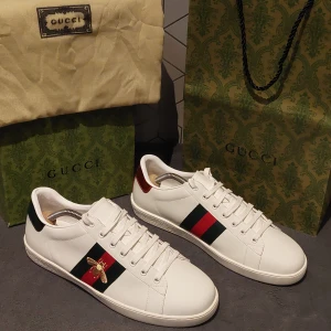 Gucci Ace skor - Säljer ett par vita Gucci Ace sneakers i skinn med klassiska gröna och röda ränder på sidorna samt broderad guldfärgad bi || Storlek 42