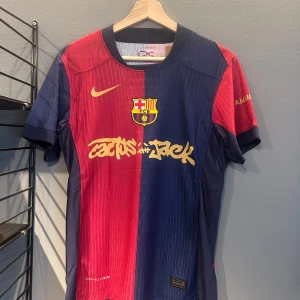 FC Barcelona x Cactus Jack matchtröja - Säljer en FC Barcelona matchtröja i samarbete med Cactus Jack. Tröjan är röd och blå med klubbmärke och Nike-logga i gult, samt tryck med Lamine Yamal och nummer 19 på ryggen. Materialet är lätt och andas, perfekt för fotboll. Helt ny med tagg en replika
