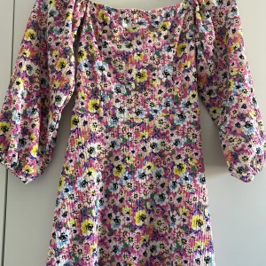 Blommig klänning med puffärmar - Superfin klänning med färgglatt blommönster i rosa, vit, gul och blå. Klänningen har puffiga långa ärmar och en lätt utställd passform. Perfekt för dig som gillar färg och vill sticka ut! Materialet är mjukt och har struktur.