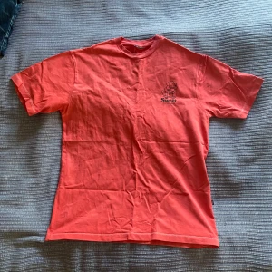 Röd t-shirt från Sweet Skateboards - Säljer en röd t-shirt från Sweet Skateboards med tryck av en glad blomma på skateboard både fram och bak. T-shirten har rund hals och korta ärmar. Tröjan var innan vit men jag har färgat den till röd då för att göra den coolare, derför är sömmarna vita.