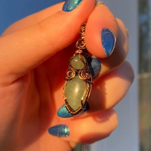 Bronsfärgad berlock med grön sten - Unik berlock med en grön, droppformad sten infattad i metalltråd i bronston. Hängs på en tunn kedja i silverfärg. Perfekt för dig som gillar bohemiska och naturinspirerade smycken. Passar till de allra flesta kedjor.