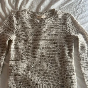 Beige stickad tröja med pärldetaljer från Hollister - Säljer en beige stickad tröja från Hollister med lång ärm och rund hals. Tröjan har små pärldetaljer broderade över hela plagget som ger en extra touch. Perfekt för dig som gillar en mysig och stilren look.