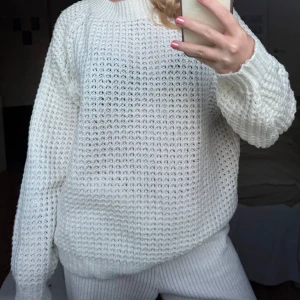Vit stickad tröja med grov struktur - Säljer en vit stickad tröja med grov, luftig struktur och rund halsringning. Tröjan har långa ärmar och breda muddar vid ärmslut och nederkant. Perfekt för lager-på-lager och enkel att styla till olika outfits.