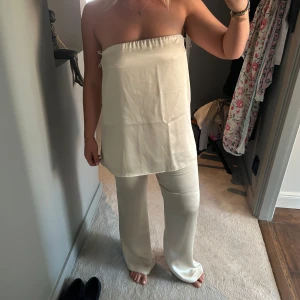 Ljusgult satin-set  - Snygga ljusgula byxor i satin med rak passform och hög midja med en matchande blus i samma färg. Aldrig använt med båda lapparna kvar! 