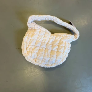 Vit quiltad axelväska från Ariana Grande Fragrances - Säljer en superfin vit quiltad axelväska från Ariana Grande Fragrances. Väskan har ett fluffigt och mjukt material, dragkedja upptill och bred axelrem. Perfekt för att bära dina viktigaste grejer med stil.