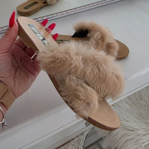 Beige fluffiga sandaler från SHEIN - Säljer ett par beige sandaler från SHEIN med mjuk, fluffig pälsimitation över foten. Skorna har platt sula och öppen tå, perfekta för en trendig och avslappnad look.