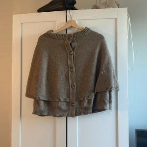 Beige stickad kofta med knappar - Mysig beige stickad kofta med knappar framtill och ribbade kanter. Koftan har en lös passform och är perfekt för lager-på-lager-stil. Passar dig som gillar en avslappnad och stilren look.