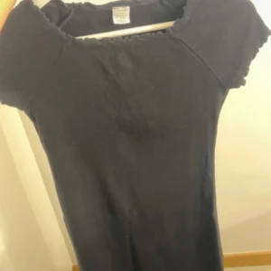 Svart kortärmad klänning från Lindex - En enkel svart klänning från Lindex med korta ärmar och rund halsringning med liten volangkant. Perfekt för en stilren look och lätt att matcha med accessoarer.