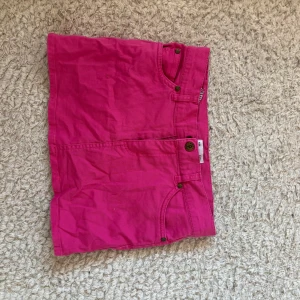 Rosa kjol  från By Elois - Säljer en knallrosa kjol s från By Elois i storlek 146. Klassisk femficksmodell med knapp och dragkedja framtill. Perfekta för sommardagar och lätta att matcha med olika toppar.