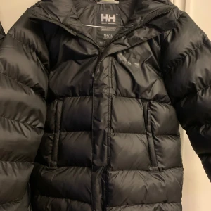 Svart vinterjacka från Helly Hansen ny pris 2300 - Säljer en svart vinterjacka från Helly Hansen den är använd ungefär 2-3 gånger inga märken eller nått, med klassisk pufferdesign. Jackan har lång ärm, dragkedja framtill och två sidofickor. Perfekt för kyliga dagar och håller dig varm hela vintern.