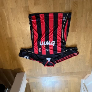 AC Milan fotbollströjor med spelarnamn - Säljer klassiska AC Milan fotbollströjor med röd-svarta ränder och guldiga detaljer. Tröjorna har spelarnamn som Pirlo, Kaká och Maldini på ryggen. Kortärmade med klubbmärke och Champions League-märke på ärmen.