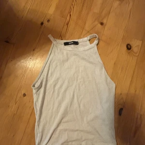 Vit ribbad linnetopp från BikBok - Säljer en vit ribbad linnetopp från BikBok. Toppen har smala axelband och hög halsringning, perfekt för varma dagar. Enkel och stilren design som passar till mycket.